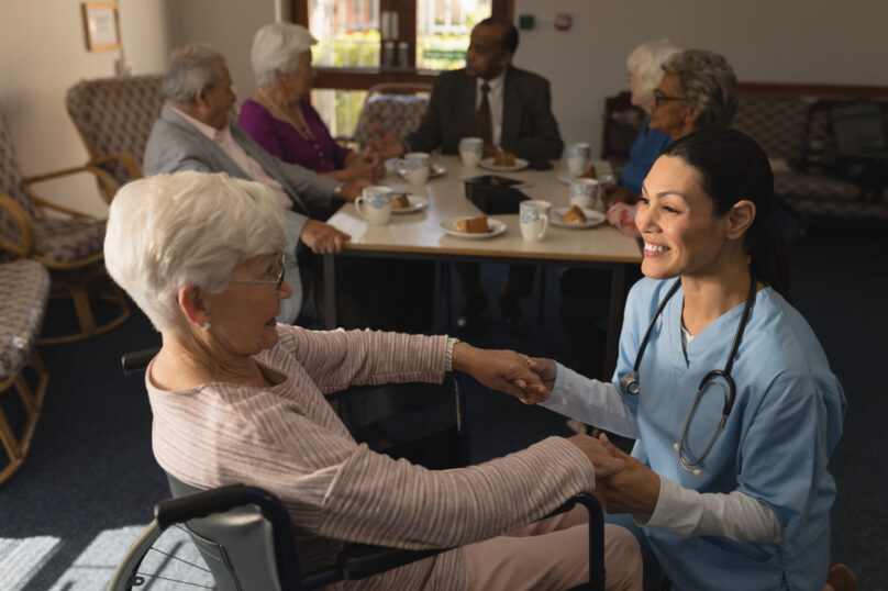Side view of happy female doctor holding hands and talking with disable senior woman at nursing home Side view of happy female doctor holding hands and talking with disable senior woman at nursing home